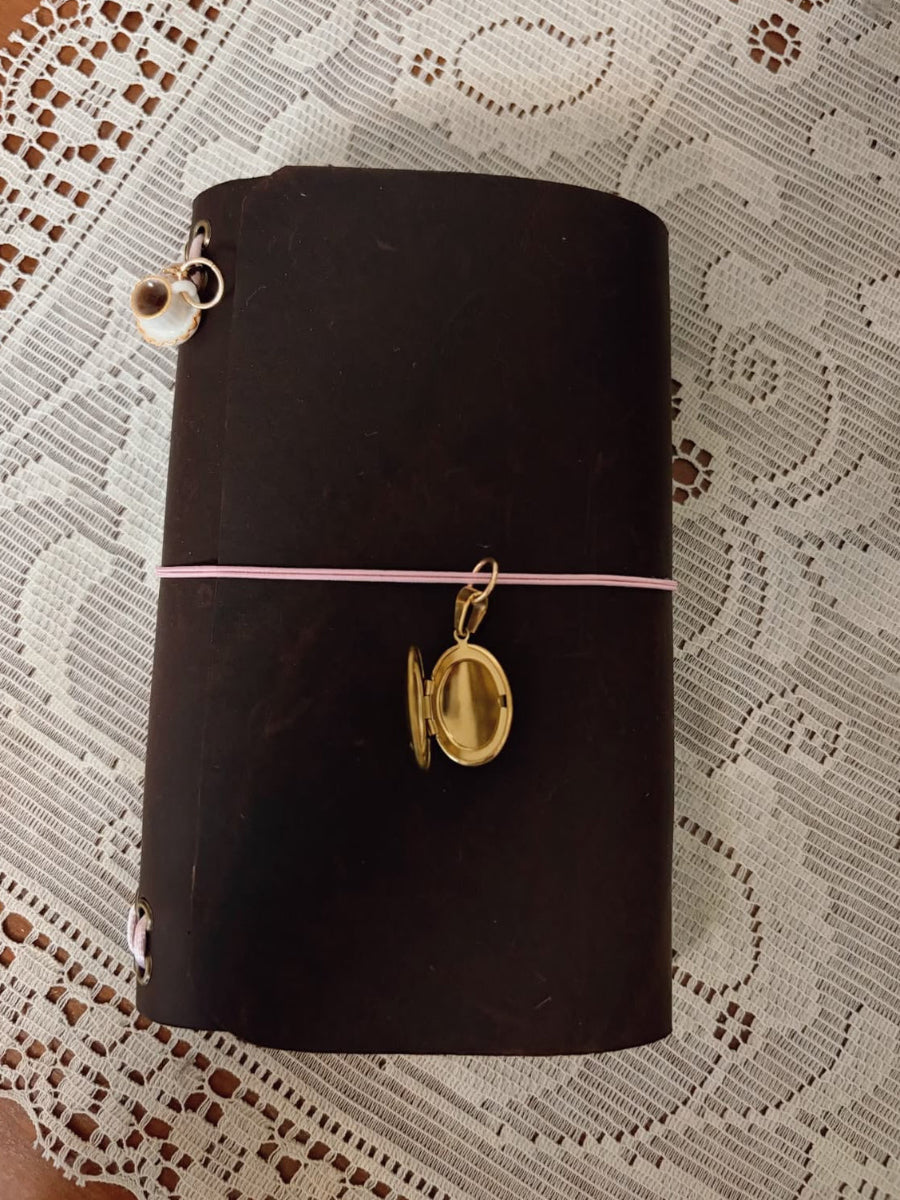 Dark brown notebook with gold charm on a lace tablecloth